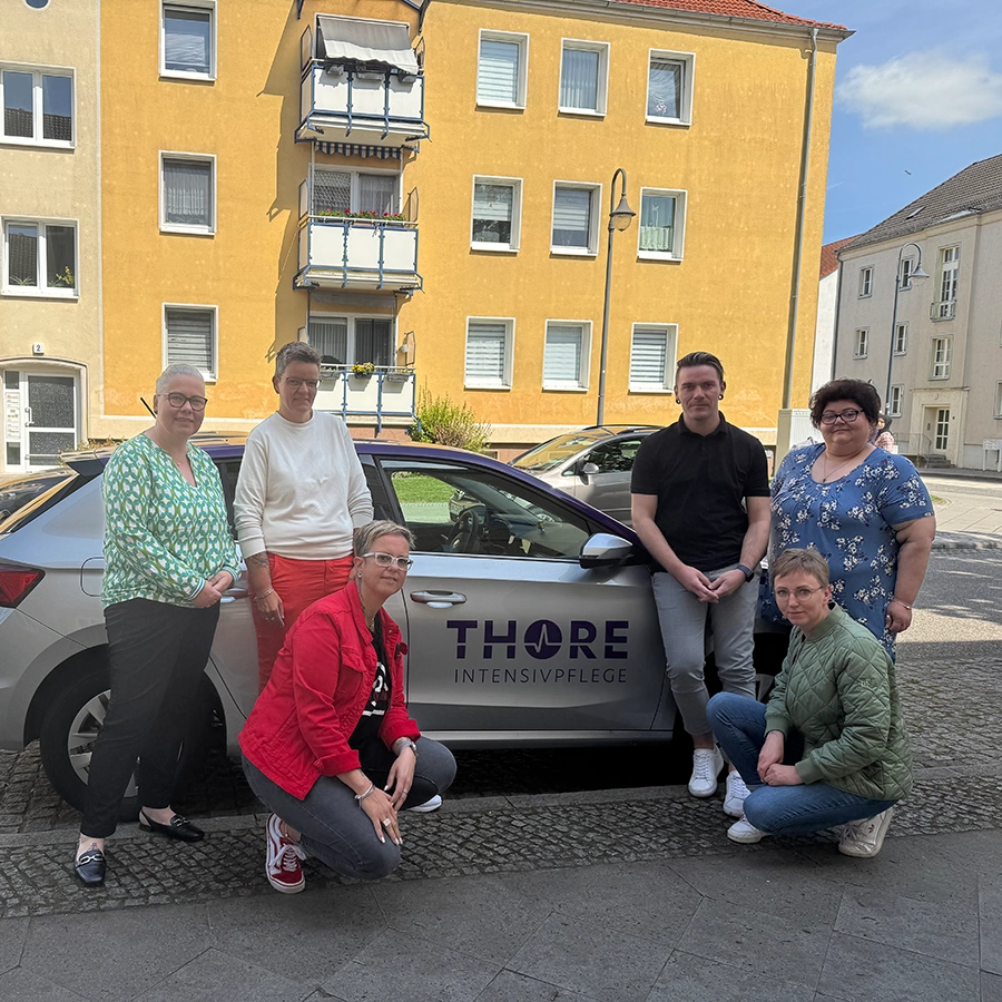 6 Mitarbeiter*innen vom Intensivpflegedienst Thore vor einem Firmenwagen posierend
