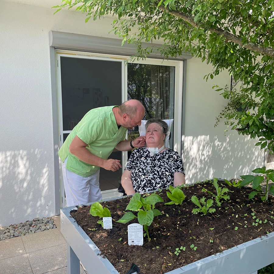 Pfleger mit Klientin draußen an einem Blumenbeet