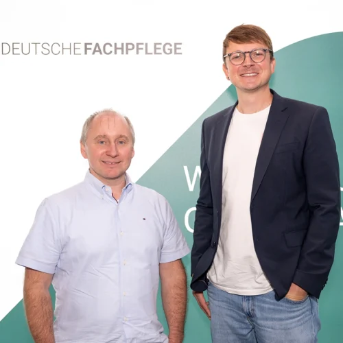 Sören Hammermüller mit mit Person vor DF-Logo-Hintergrund in die Kamera lächelnd