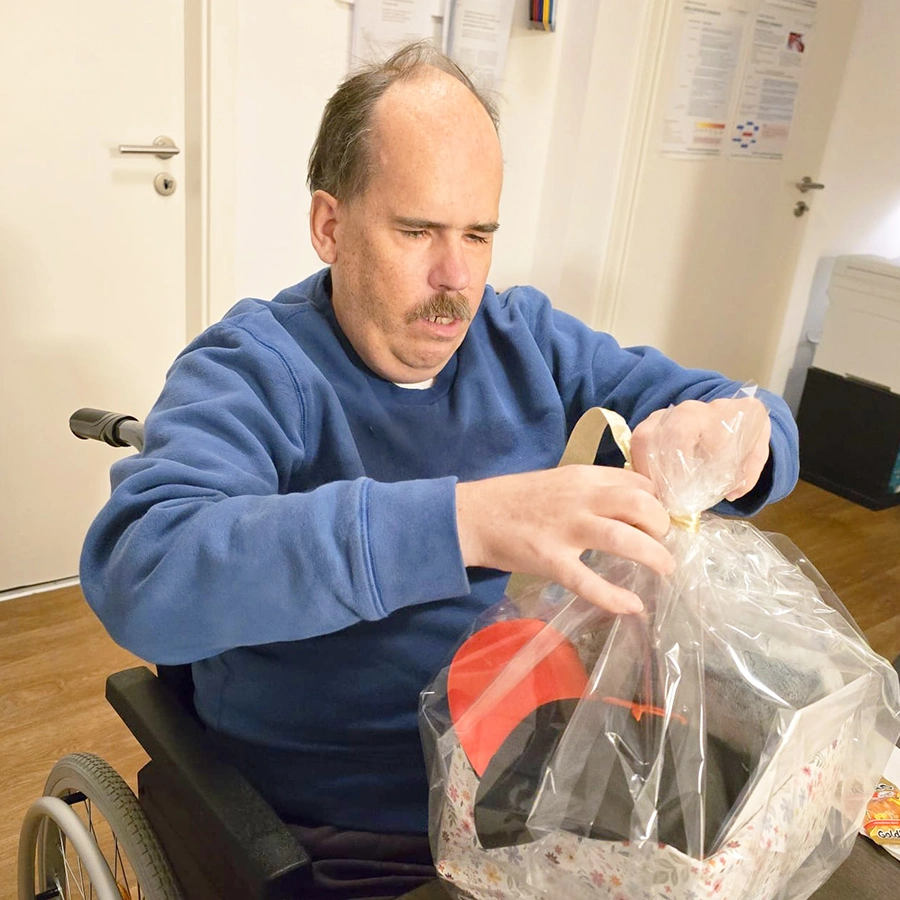 Uwe im Rollstuhl im Zimmer mit einer Tüte in der Hand,