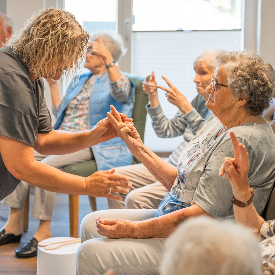 Mehrere Klientinnen im Raum, die Fingerübungen mit einer weiblichen Pflegekraft durchführen.