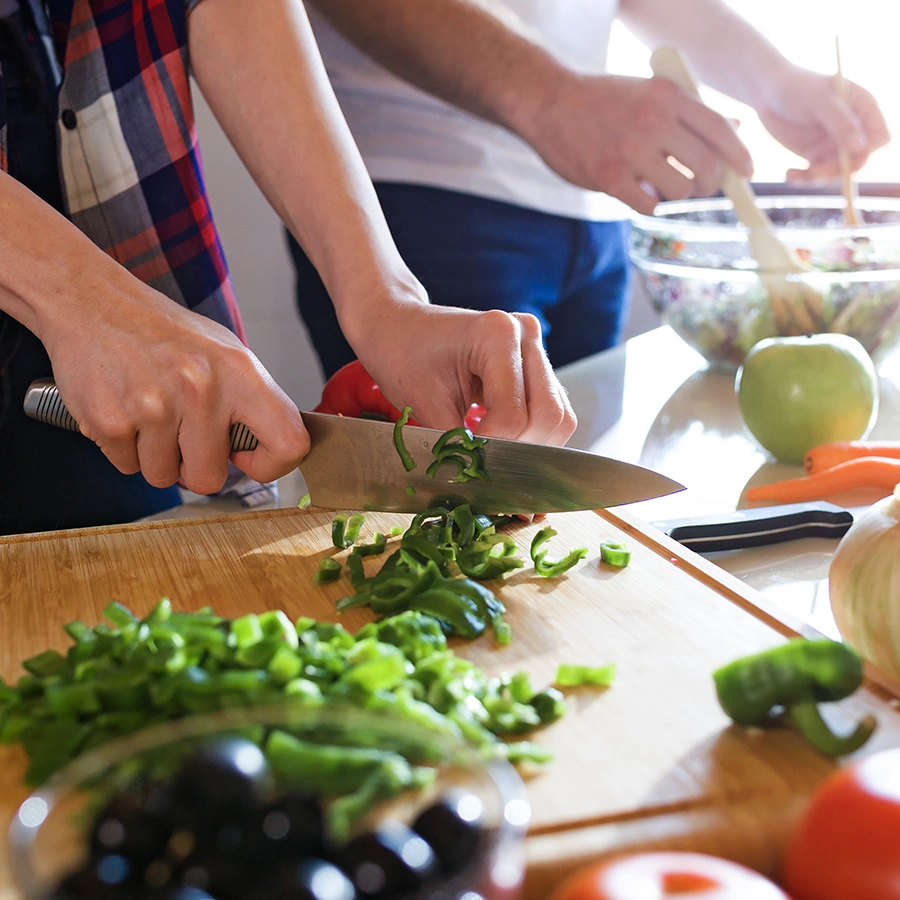 2 Personen bereiten Essen vor. Ansicht mit Fokus auf die Hände. Es wird Gemüse geschnippelt.