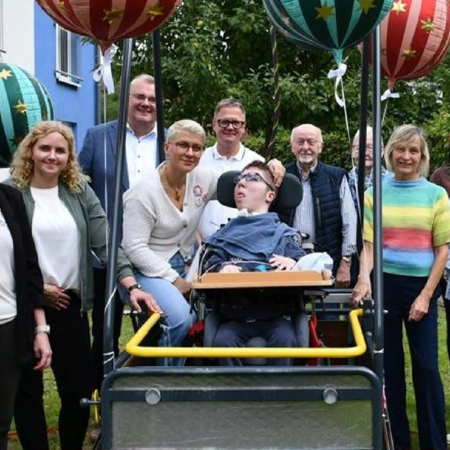 Das Team und ein Kind auf der neuen Schaukel im Garten lächeln in die Kamera.